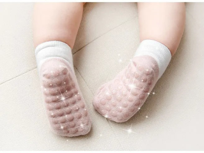 Toddler crawling wearing white and pink socks with glittery grid of grips under the sole.